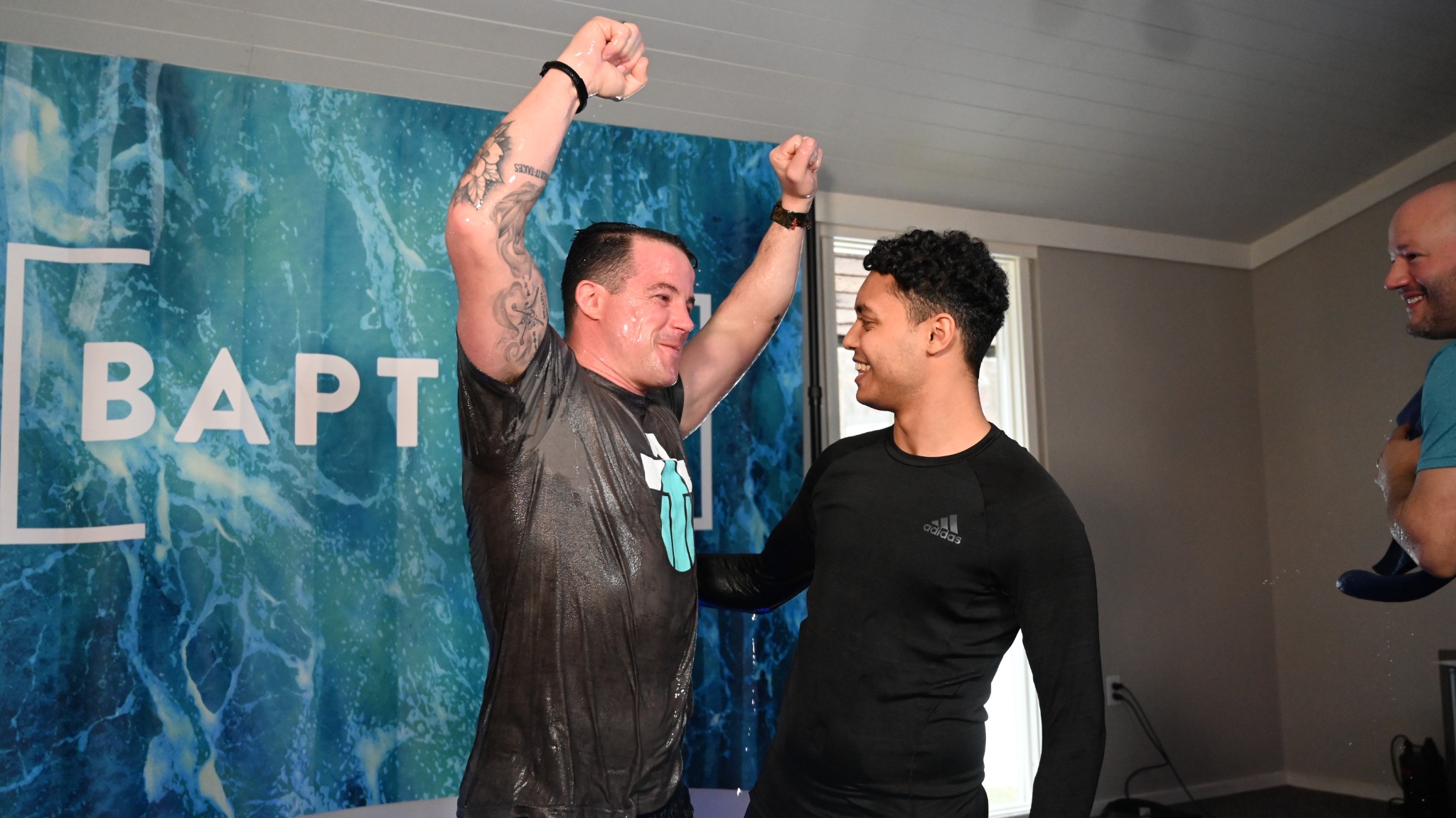 A man raises both arms in celebration after his water baptism at Broad River Church.