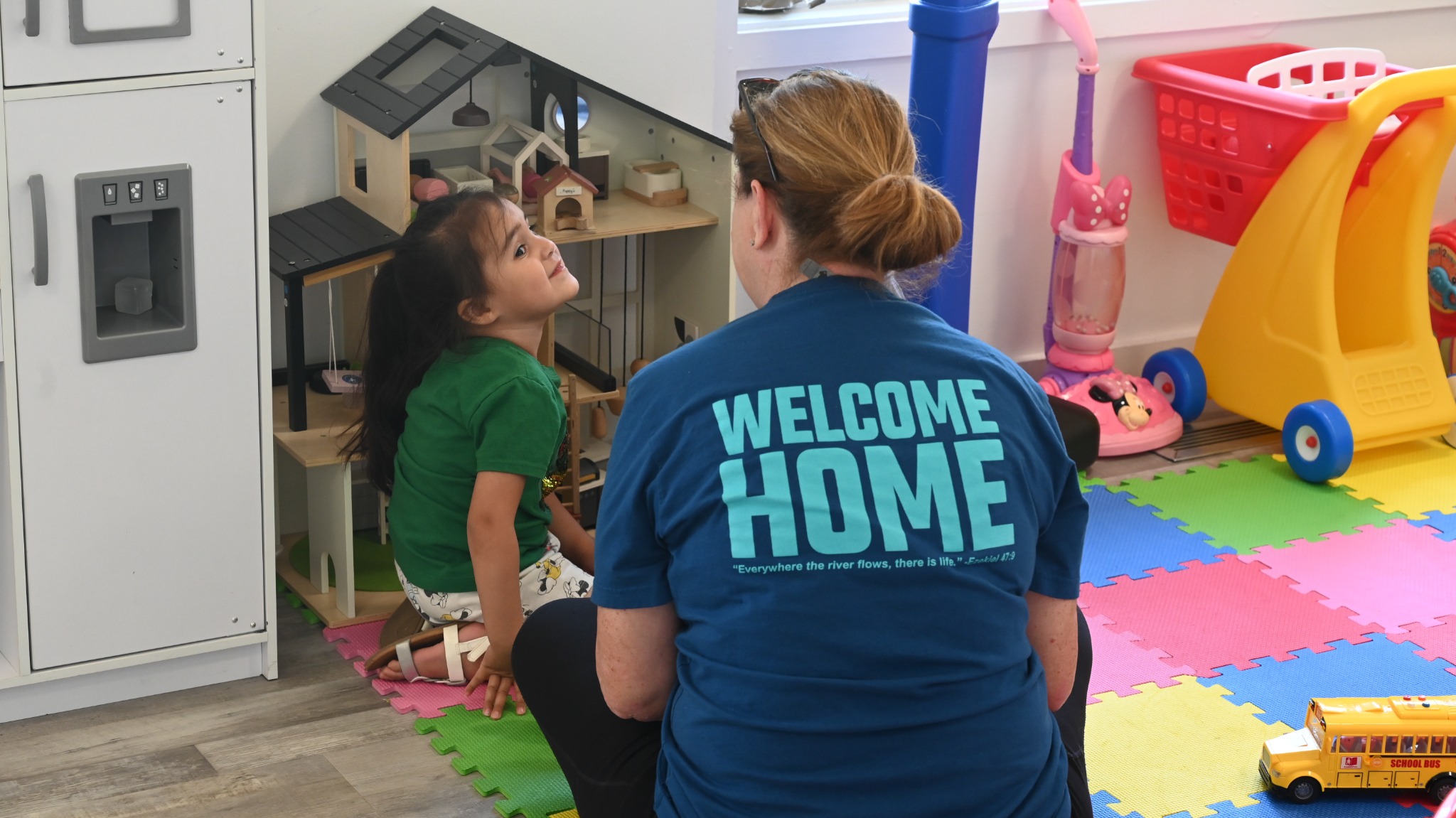 A teacher playing alongside a young child in a colorful playroom