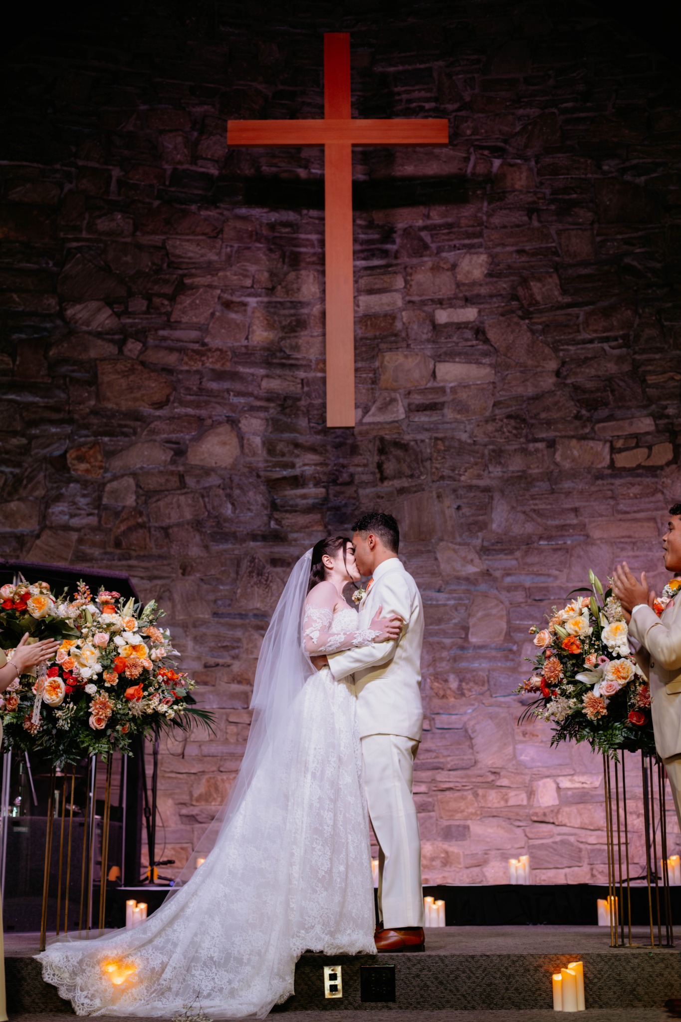 Bride and groom kissing beneath the cross and stone backdrop