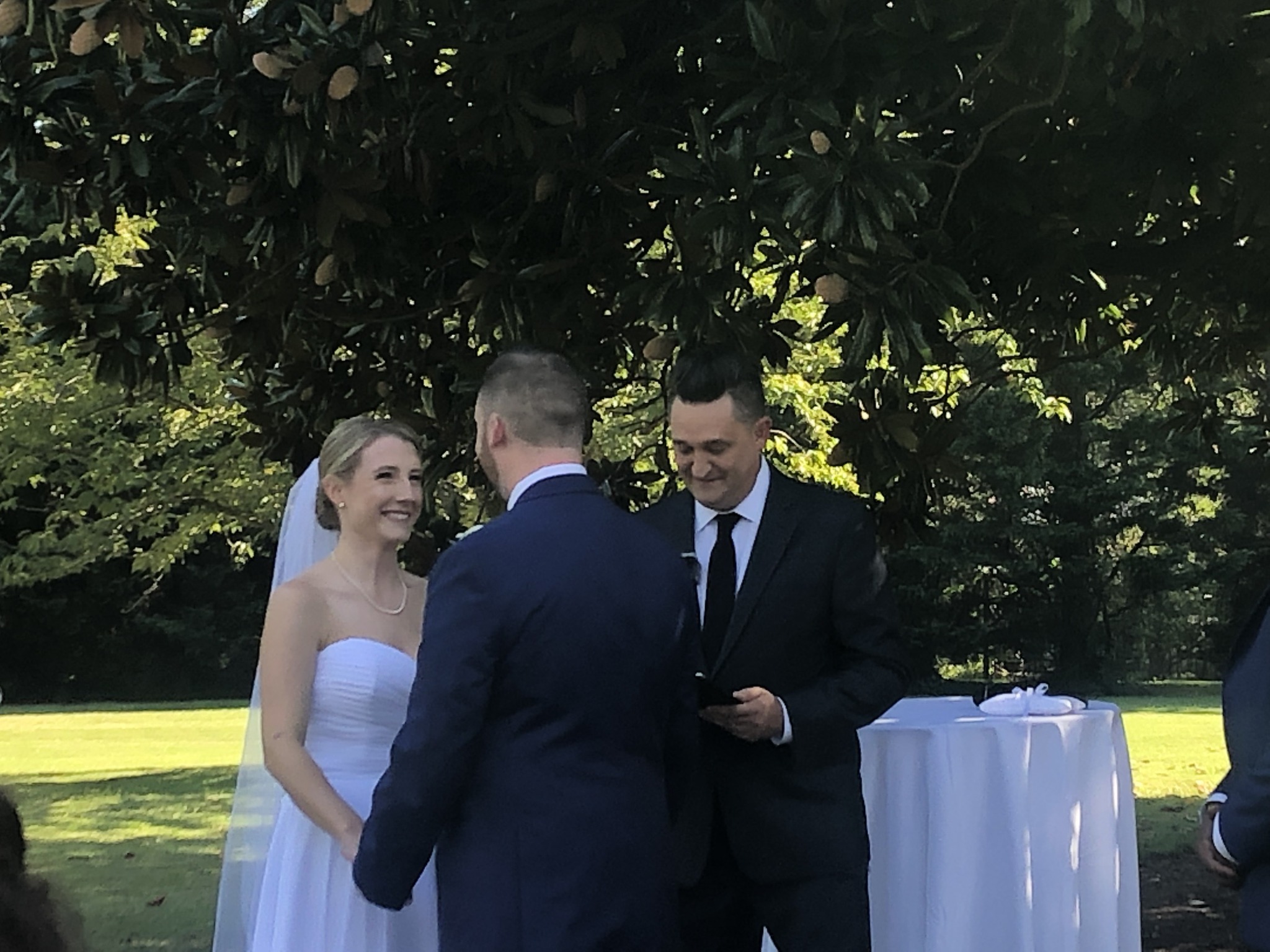 Kevin officiating an outdoor wedding as the bride smiles at her groom