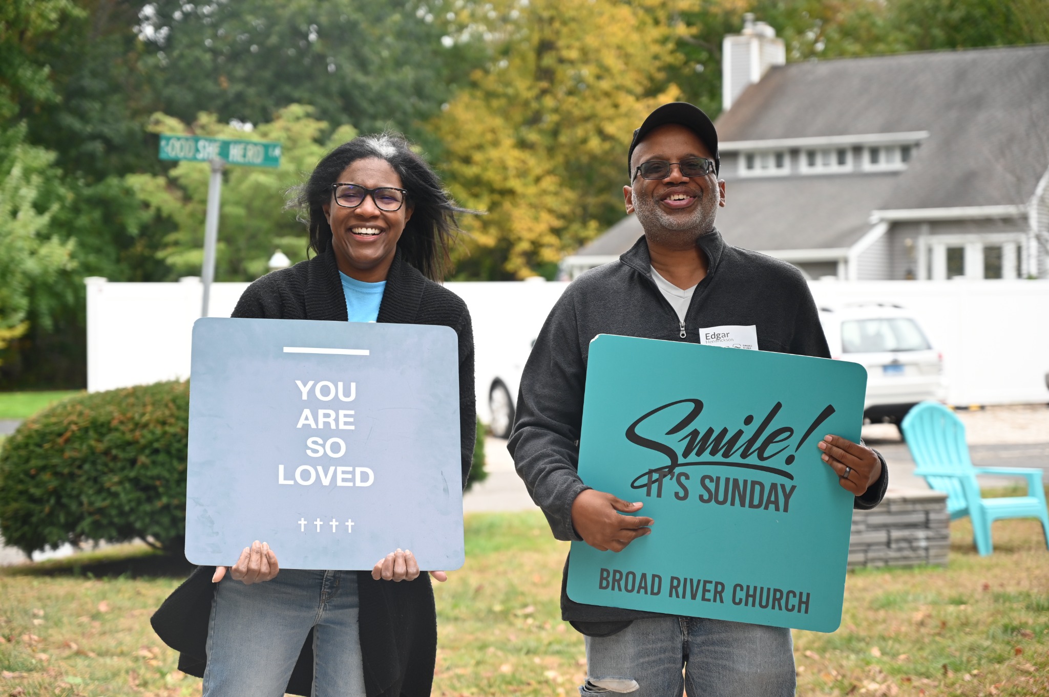 Two smiling volunteers holding welcome signs outside Broad River Church.