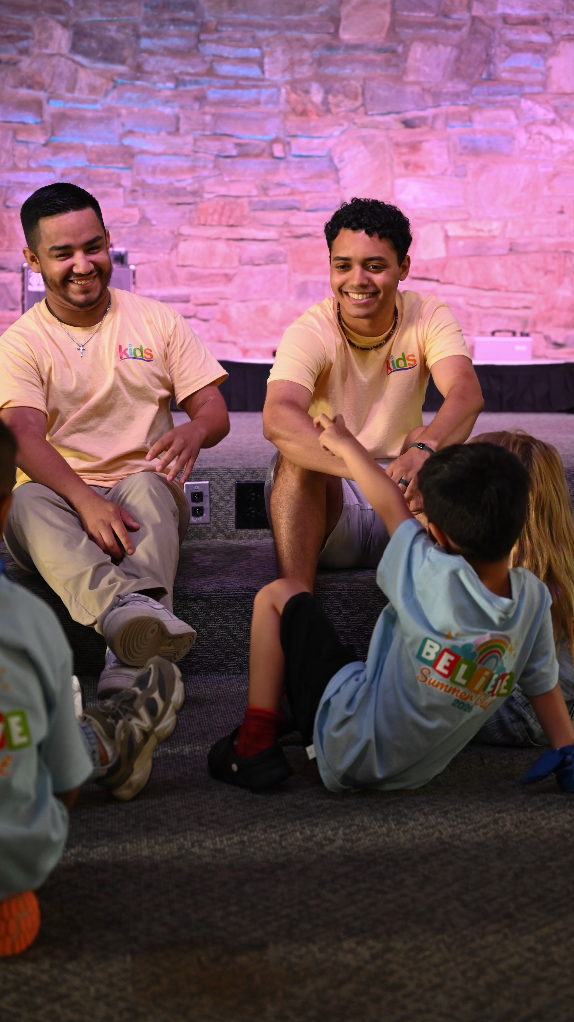 Two Kids volunteers sitting with children and listening during a group activity.