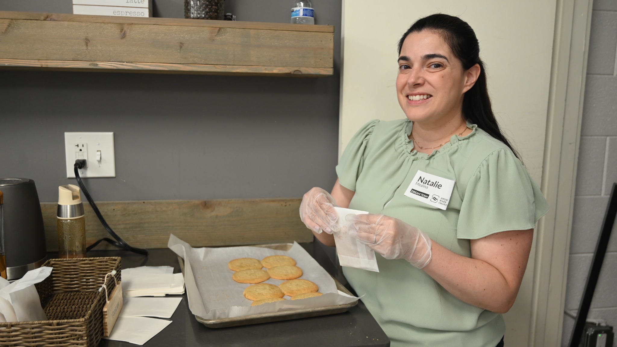 A café volunteer preparing cookies with food-service gloves.