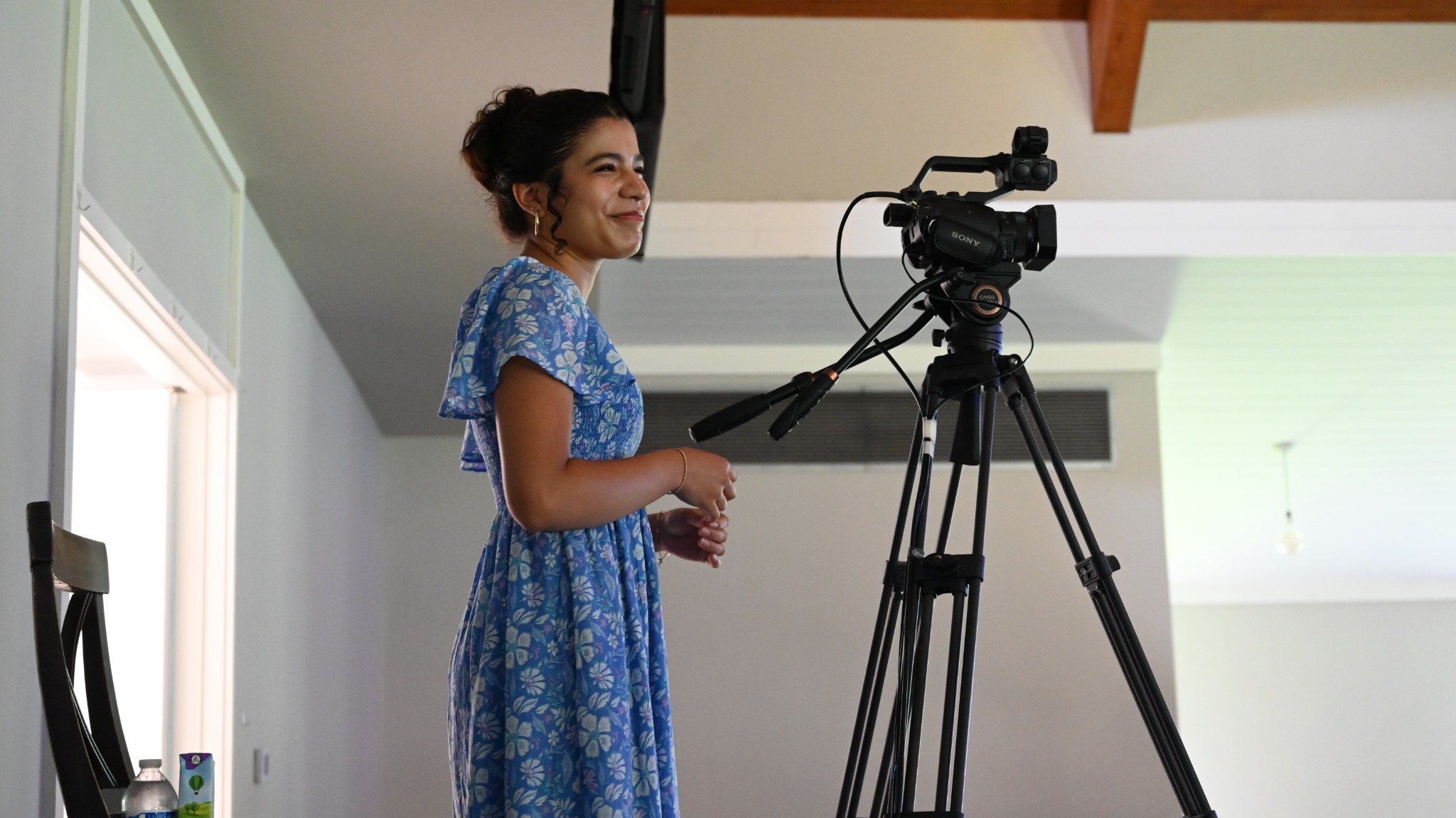 A smiling volunteer standing beside a video camera on a tripod.