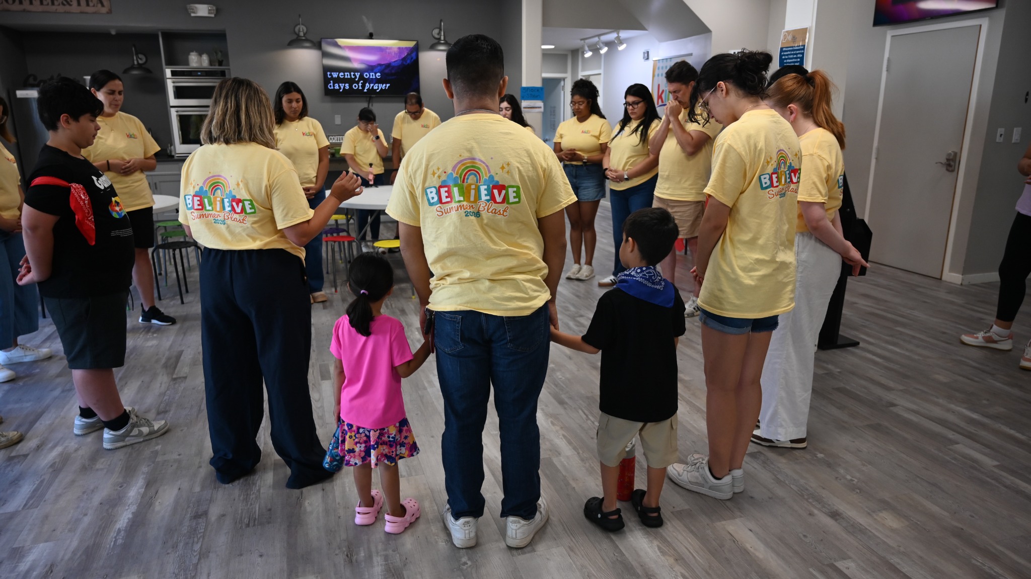 Kids volunteers and children gathered in a circle with bowed heads.