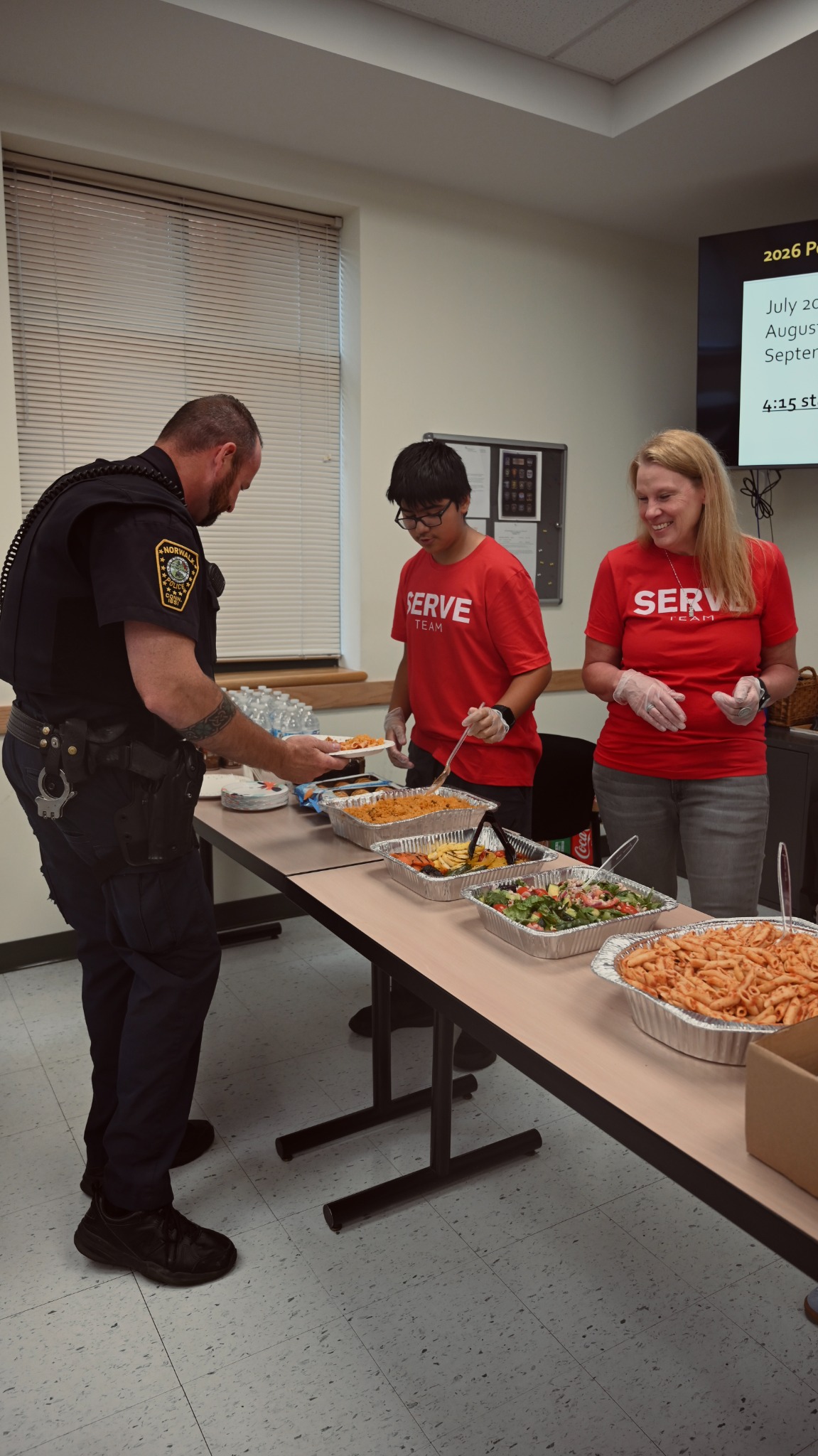 Two Serve Team volunteers serving a meal to a uniformed police officer.