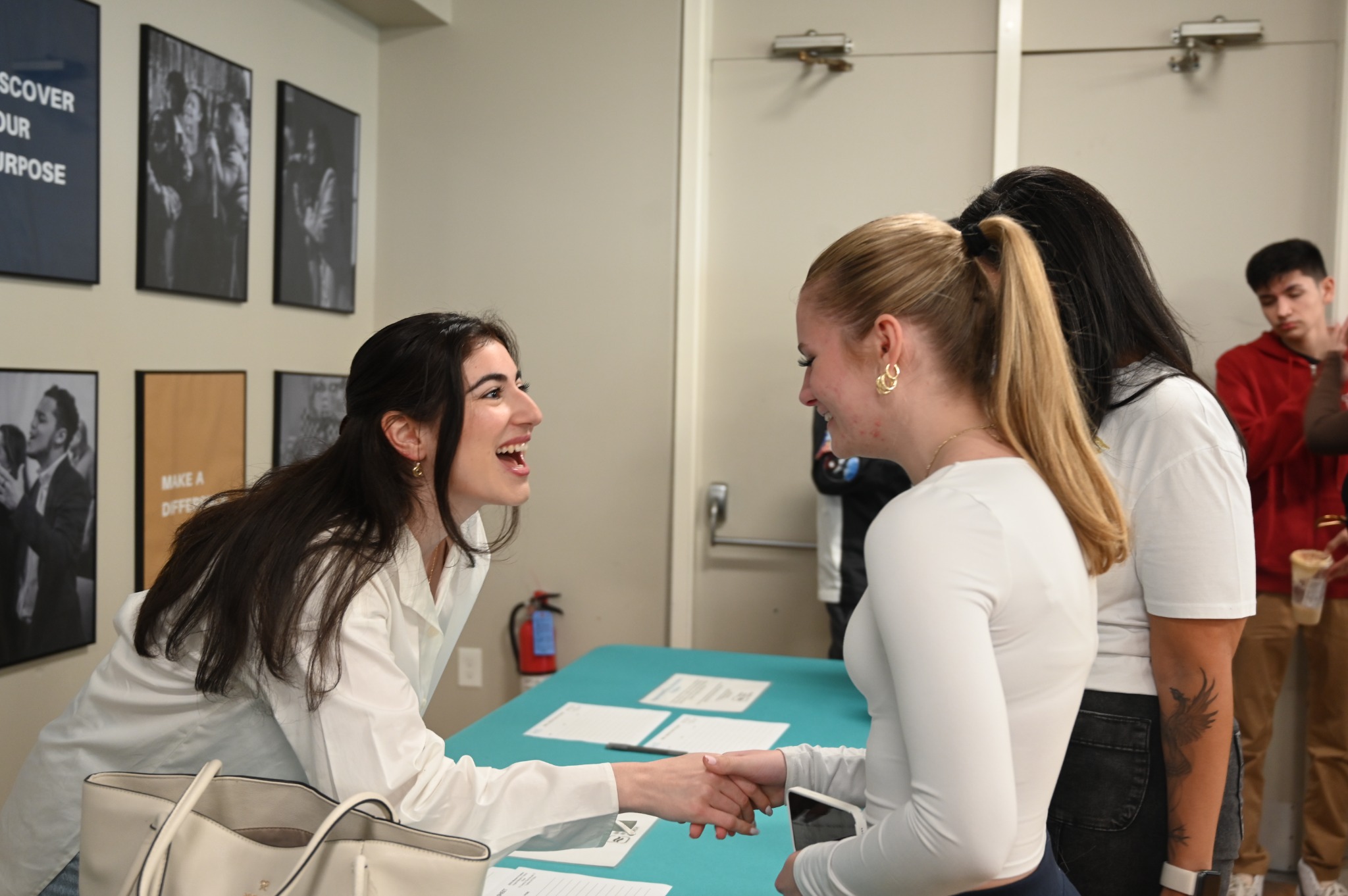 Two people smiling and shaking hands across a welcome table.
