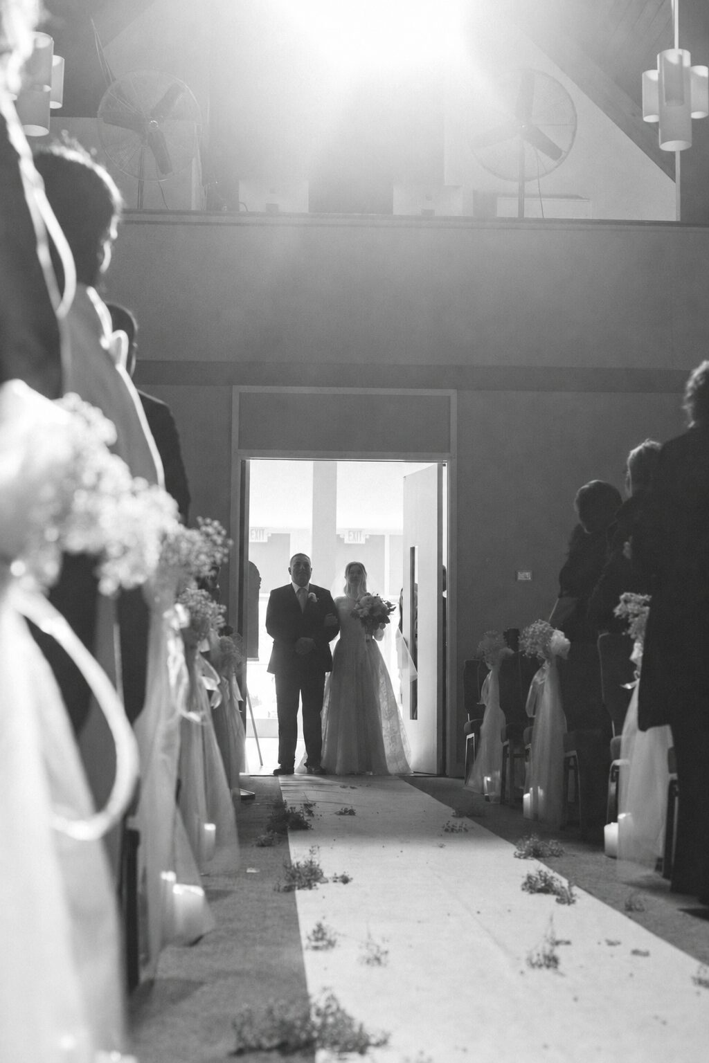 Bride and escort entering through the rear doors along a candlelit aisle